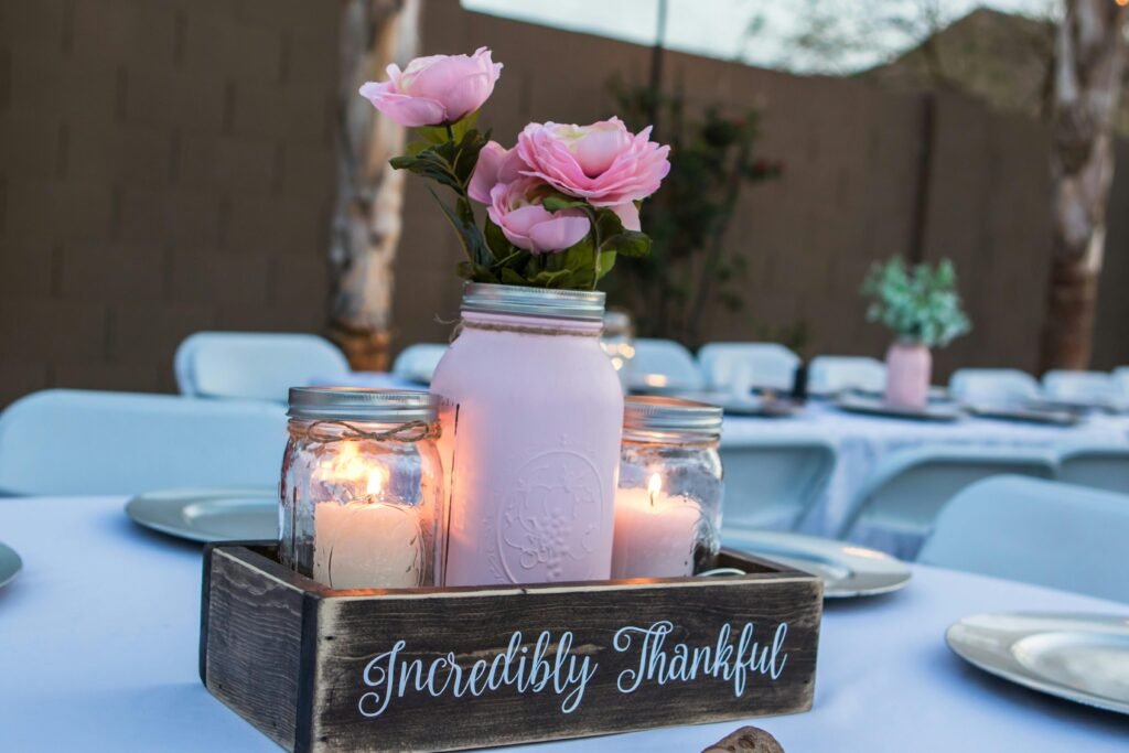 A beautiful centerpiece with pink roses and candles in mason jars, set on a decorated outdoor table.