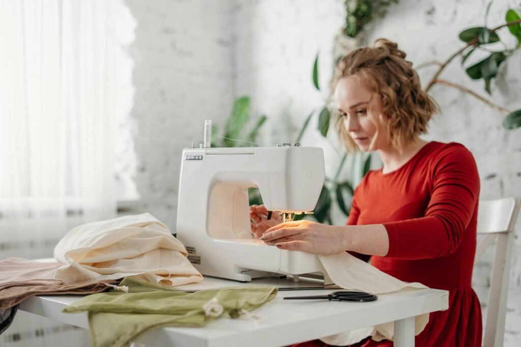 A woman in a red dress using a sewing machine at home, creating a handmade garment.