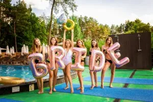 A fun bachelorette party by the pool with six women holding 'BRIDE' balloons, enjoying the summer sun.