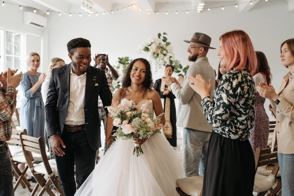 A joyful couple exits the ceremony as guests applaud during their wedding indoors.